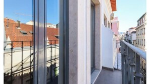 Ein Balkon mit Metallgeländer, ein klarer Himmel und Gebäude im Hintergrund.