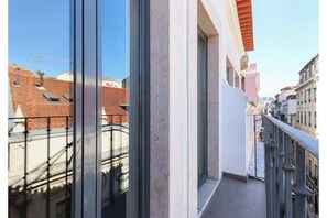 Un balcon avec une rambarde en métal, un ciel dégagé et des bâtiments en arrière-plan.