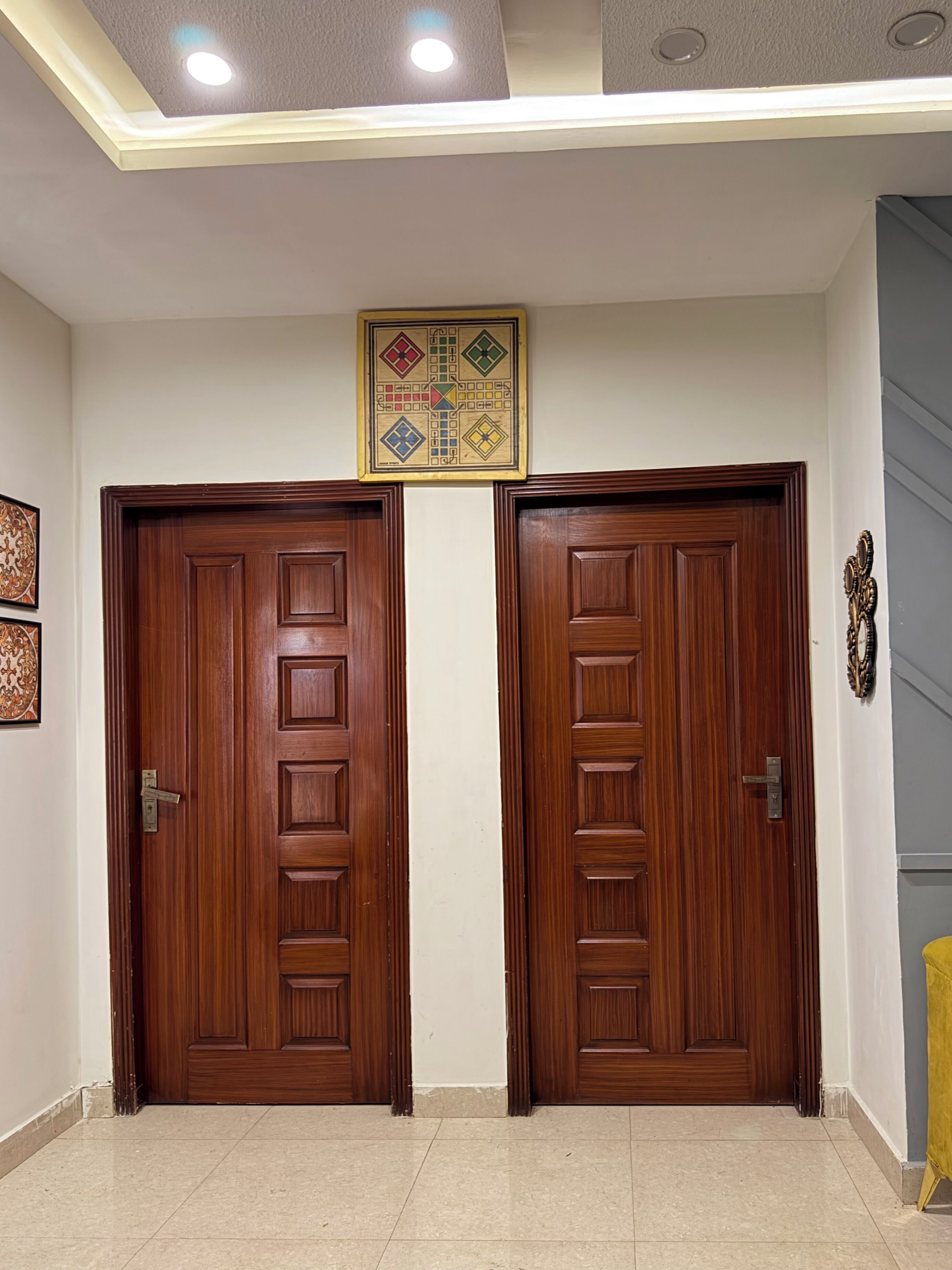 Un corridoio con due porte in legno, una lampada a soffitto e un quadro appeso sopra le porte.