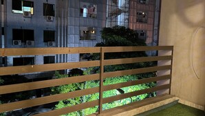 Ein Balkon mit Holzgeländer, künstlichem Rasen und Blick auf ein Gebäude mit zahlreichen Fenstern und Klimaanlagen.