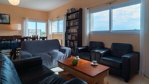 Un salon comprenant un canapé, deux fauteuils, une table basse, une bibliothèque et un coin repas avec une table et des chaises.