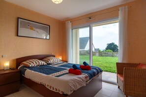 Een slaapkamer met een bed, een nachtkastje, een rieten stoel en een groot raam.