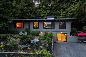 Ein modernes, zweistöckiges Haus mit einem gepflegten Garten, einer Terrasse mit Gartenmöbeln und einer sichtbaren Garagentür.