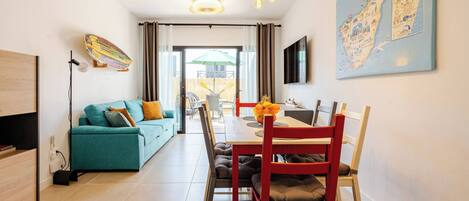 Een moderne woonkamer met een bank, eettafel, stoelen en een aan de muur bevestigde televisie.