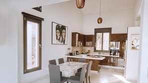 Een moderne keuken met een eethoek, met een marmeren tafel, donkere stoelen en een groot schiereiland met een spoelbak.