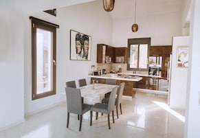 Una cocina moderna con comedor, que presenta una mesa de mármol, sillas oscuras y una isla grande con pileta.