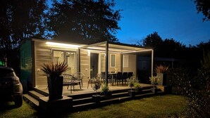 Ein modernes, helles Haus mit Terrasse, Sitzgelegenheiten im Freien und Topfpflanzen.