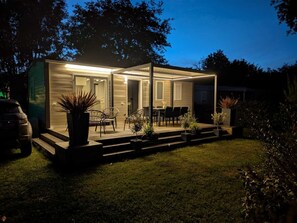 Ein modernes, helles Haus mit Terrasse, Sitzgelegenheiten im Freien und Topfpflanzen.