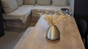 Ein modernes Zimmer mit einem Holzesstisch, einer schwarzen Pendelleuchte, einer Couch mit beige farbenen Kissen und einem Fenster mit gemusterten Vorhängen.