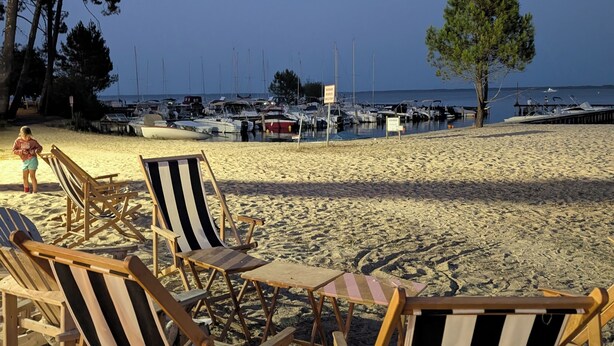 Strandstühle, ein Baum und Boote im Hintergrund.