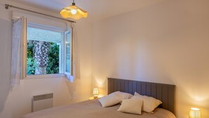 Een slaapkamer met een bed, nachtlampjes, een raam met gordijnen en een radiator.