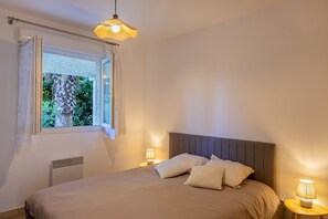 Ein Schlafzimmer mit Bett, Nachttischlampen, einem Fenster mit Vorhängen und einer Heizung.