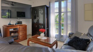 Een woonkamer met een flatscreen televisie, een houten kast, glazen deuren en een bank met een zwart kussen.