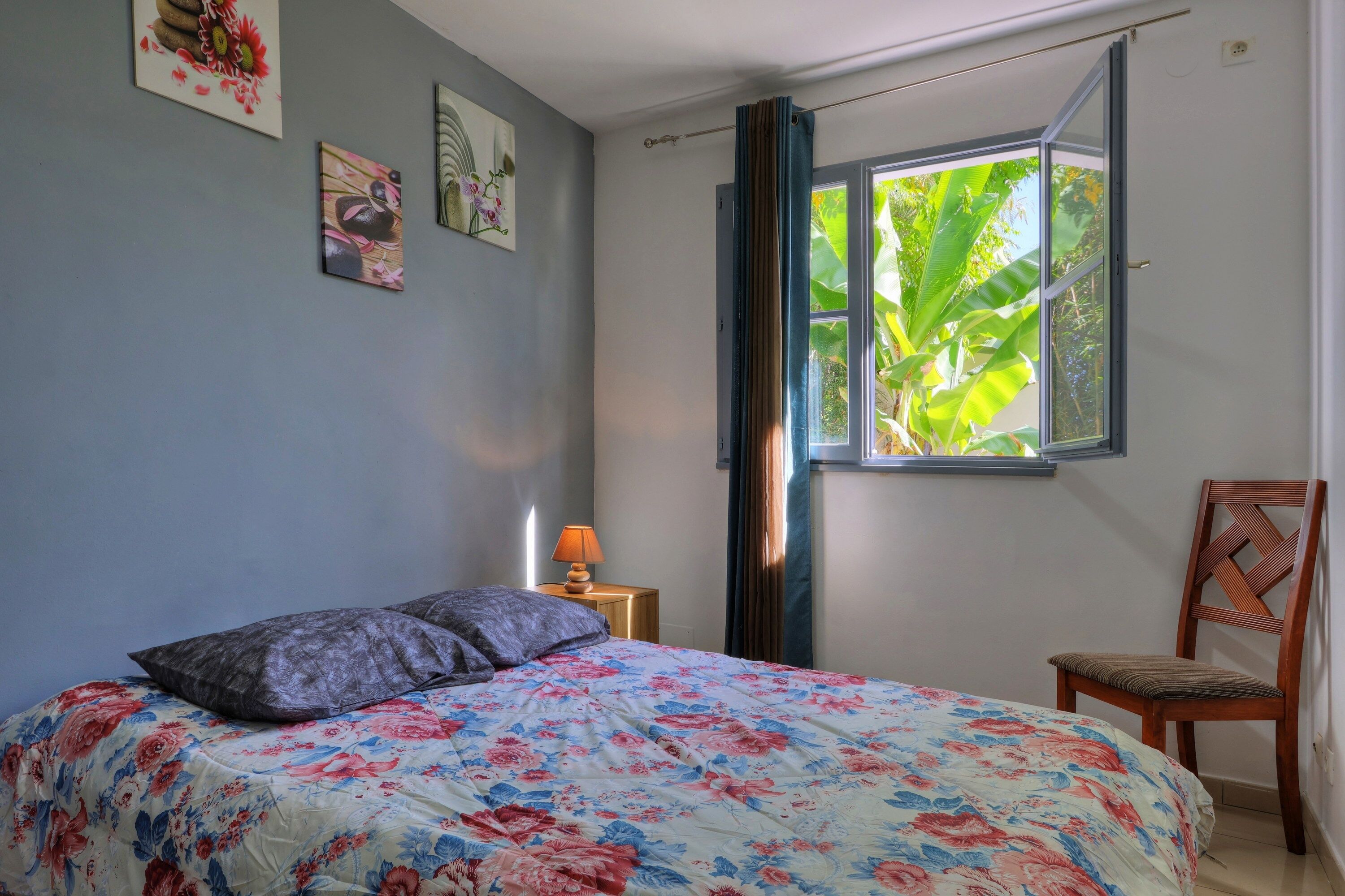 Un dormitorio con cama, una silla, un ventanal con cortinas y decoración en la pared.