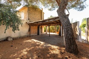 Ein rustikales Steinhaus mit überdachter Terrasse, einem Baum und Kiesgrundstück.