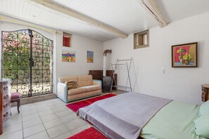 Et soveværelse med seng, sofa, radiator og et vindue med metalgitter.