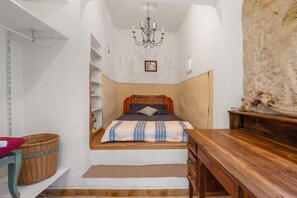 Ein Schlafzimmer mit einem Bett, einem hölzernen Schminktisch, einem Korbwannen und einem Kronleuchter.