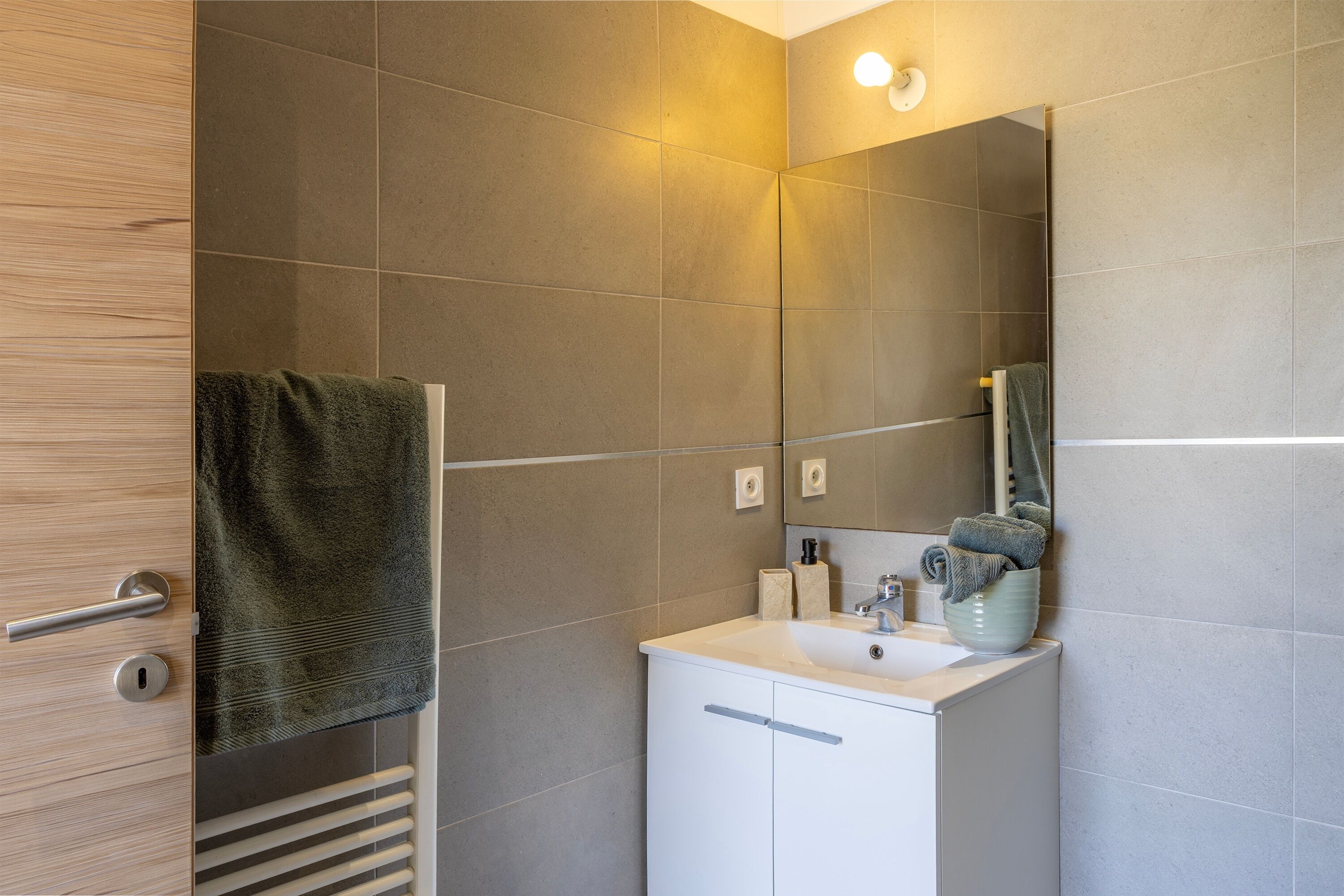 A bathroom with a mirror, sink, towel rack, and a towel hanging on the door.