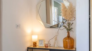 Ein Spiegel mit geometrischer Rahmung, eine Vase mit getrocknetem Pampasgras, ein gerahmtes Zertifikat und eine Lampe auf einer Holzkonsole.
