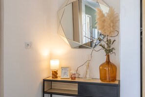Ein Spiegel mit geometrischer Rahmung, eine Vase mit getrocknetem Pampasgras, ein gerahmtes Zertifikat und eine Lampe auf einer Holzkonsole.