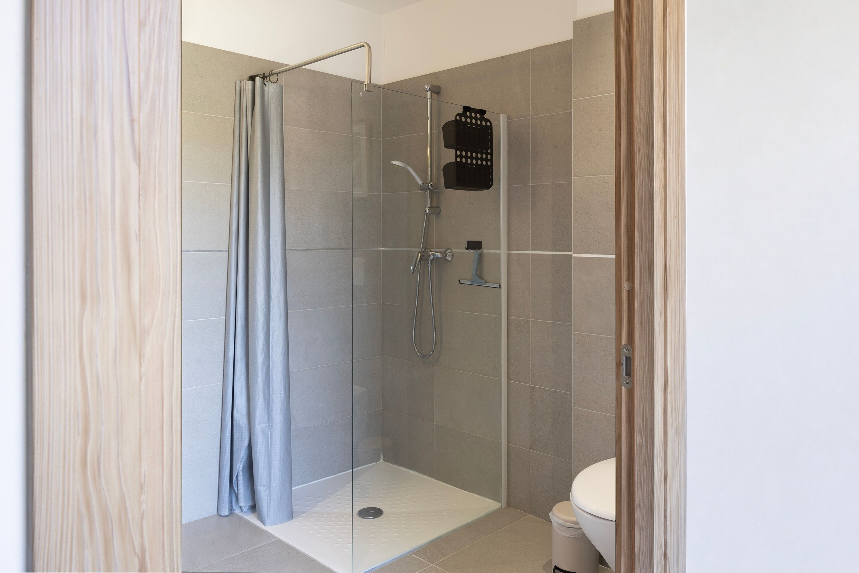 Une douche avec une porte en verre, un pommeau de douche et un flexible de douche.