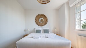 Cama bem arrumada com lençóis brancos, duas almofadas e um enfeite de parede.