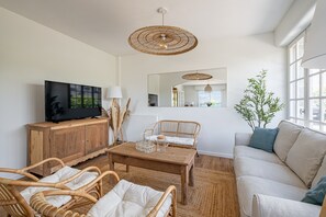Ein Wohnzimmer mit Fernseher, Korbmöbeln, einem Holztisch und einem großen Fenster.