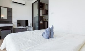Habitación de hotel con cama, escritorio, silla, televisor, refrigerador y puerta corrediza que da a una kitchenette.