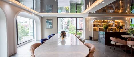 A modern interior with a long dining table, seating, and a kitchen area.