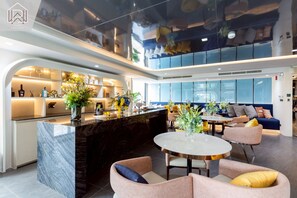 A modern hotel lobby with a marble reception desk, seating area with sofas, and a large window offering a city view. - Modern Cozy Condo in Ratchada 36 Perfect for 10+ Nights (Krung Thep Maha Nakhon)