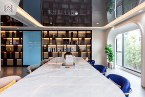 A modern interior with a long marble table, blue chairs, a bookshelf, and a large window. - Modern Cozy Condo in Ratchada 36 Perfect for 10+ Nights (Krung Thep Maha Nakhon)