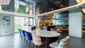 A modern interior with a central island table, seating, and a view of the outside. - Modern Cozy Condo in Ratchada 36 Perfect for 10+ Nights (Krung Thep Maha Nakhon)