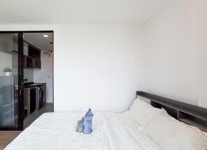 A bedroom with a bed, a small kitchenette, and a glass door leading to a bathroom. - Уютная современная квартира в Ратчада От 10 ночей и более (Krung Thep Maha Nakhon)