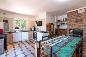 Een keuken met betegelde vloer, witte kasten, een houten eettafel en een bakstenen muur.