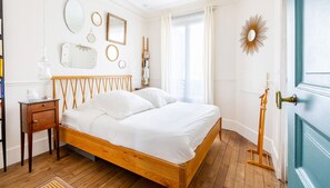 A bedroom with a wooden bed, a bedside table, a mirror, and a door with a handle. - Montmartre Sacré Coeur - Superbe appart pour 2 (Paris)