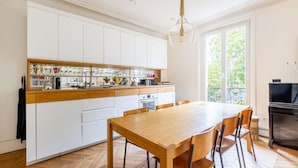 A modern kitchen with white cabinets, a wooden countertop, and a dining table with chairs. - Montmartre Sacré Coeur - Superbe appart pour 2 (Paris)