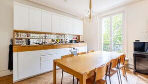 A modern kitchen with white cabinets, a wooden countertop, and a dining table with chairs. - Montmartre Sacré Coeur - Superbe appart pour 2 (Paris)
