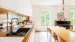 A modern kitchen with a wooden countertop, a sink, and a dining area with a table and chairs. - Montmartre Sacré Coeur - Superbe appart pour 2 (Paris)
