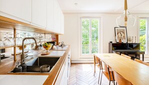 A modern kitchen with a wooden countertop, a sink, and a dining area with a table and chairs. - Montmartre Sacré Coeur - Superbe appart pour 2 (Paris)