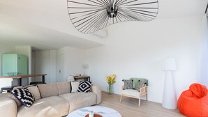 Ett modernt vardagsrum med en soffa, ett soffbord, en sittpuff, en lampa och en taklampa.
