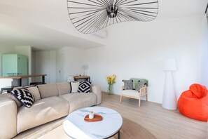 Een moderne woonkamer met een bank, een salontafel, een relax fauteuil, een lamp en een plafondarmatuur.