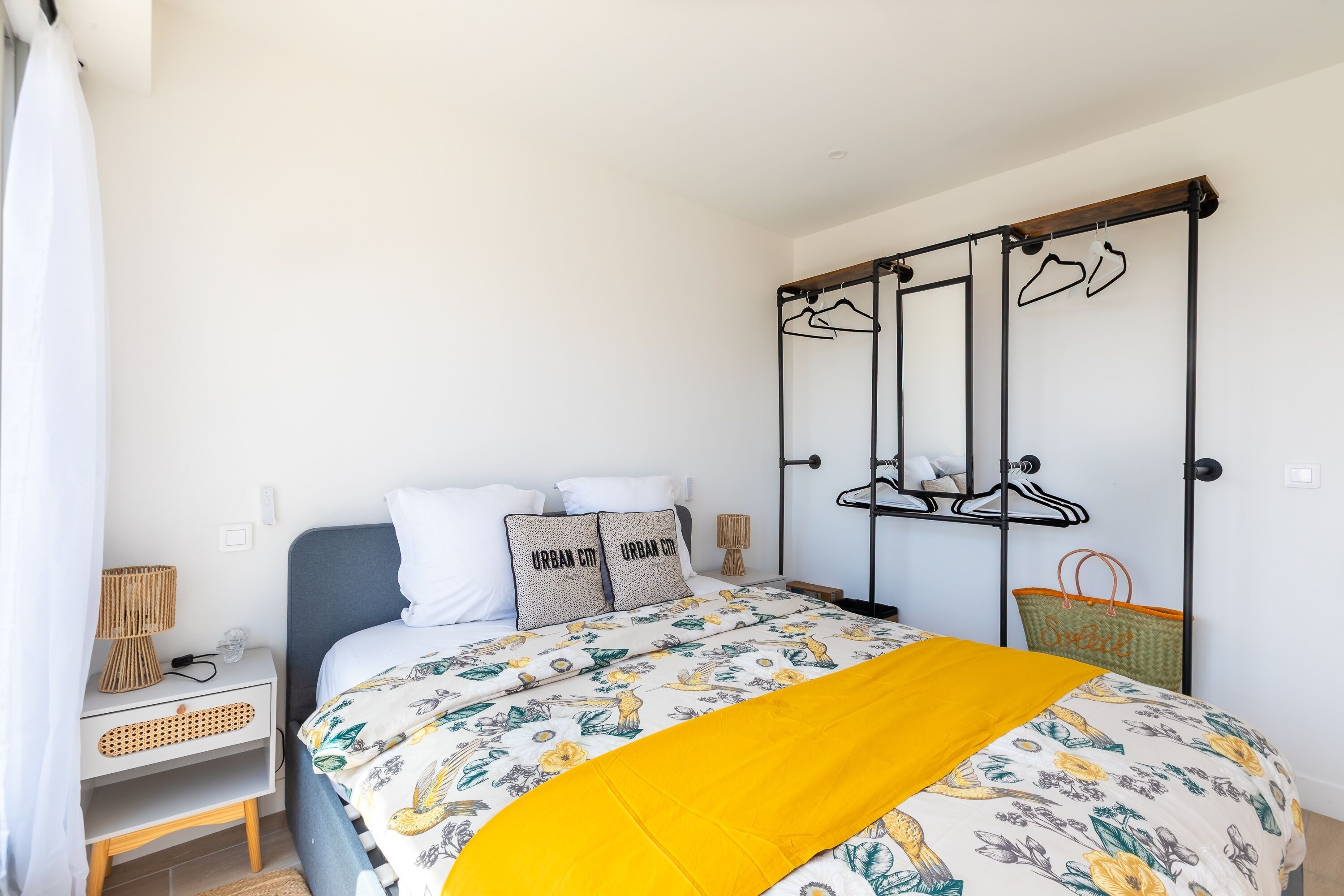 Een slaapkamer met een bed, een nachtkastje, een kapstok en een wandplank.