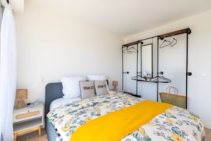 Ein Schlafzimmer mit einem Bett, einem Nachttisch, einem Kleiderhaken und einem Wandregal.