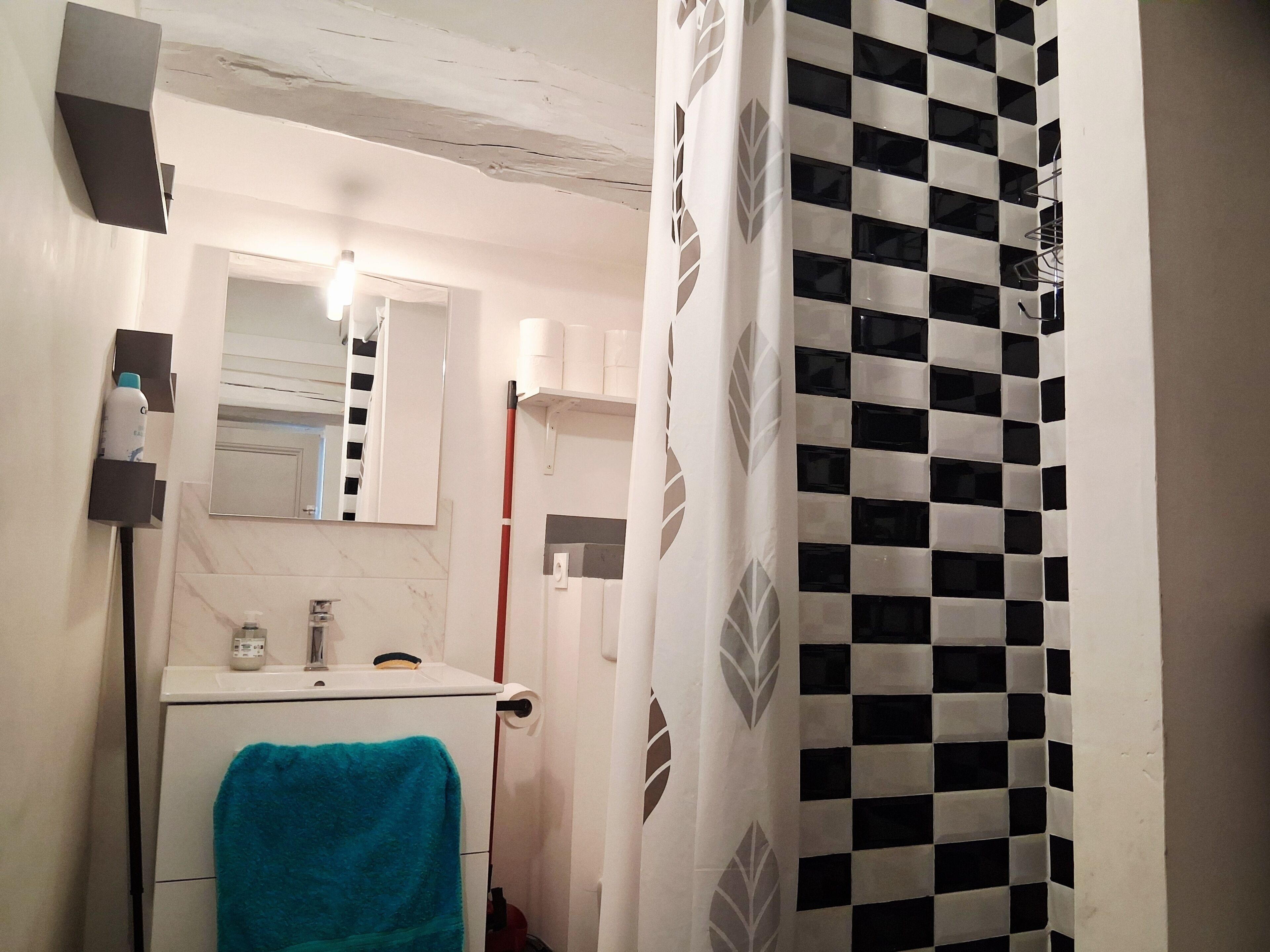 A bathroom with a sink, mirror, towel rack, and a checkered shower curtain.