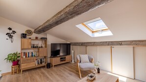A loft-style room with a skylight, wooden flooring, a TV, bookshelves, a chair, and a small table. - La Terrasse de Vidauban - Duplex climatisé (Vidauban)