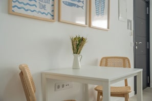 A white table with a vase of dried plants, two wicker chairs, and framed wall art depicting fish and waves. - Cozy Apartment Rental in Guargacho, Spain - Ideal Family Stay (Arona)