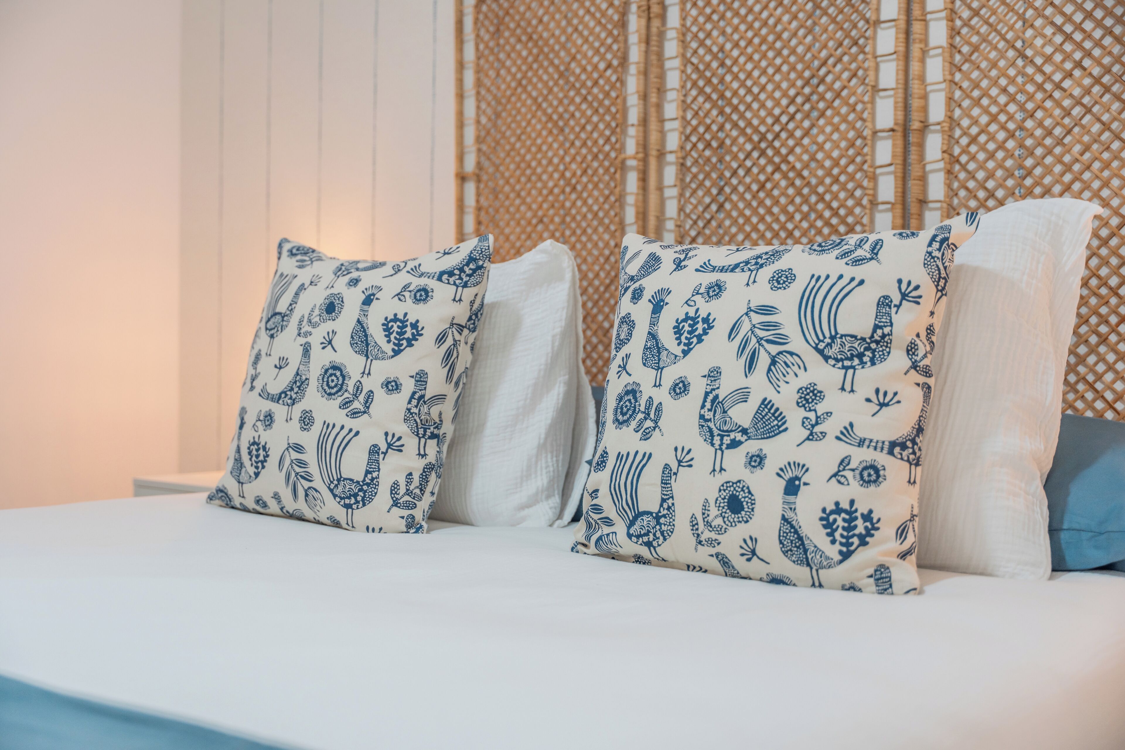 A bed with two pillows, one with a blue pattern and the other plain, in a room with a bamboo wall.