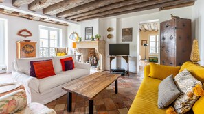 Una sala de estar con un sofá blanco, un sofá amarillo, una mesa de centro de madera, una chimenea, un televisor y un mueble grande.