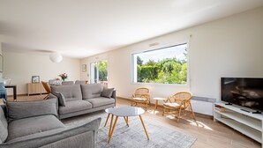Ett modernt vardagsrum med en soffa, fåtöljer, en tv och stora fönster.