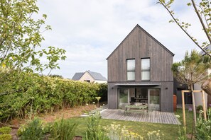 Een modern huis met een houten gevel, een terras en een tuin met verschillende planten en bloemen.